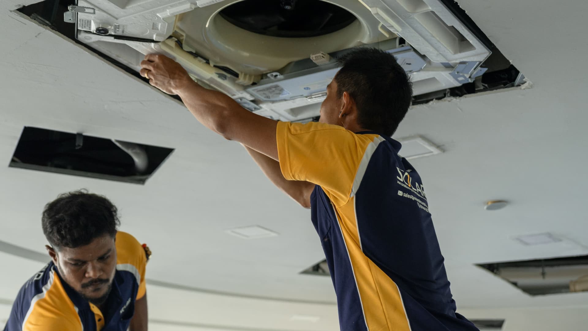 two saces staff servicing a ceiling aircon